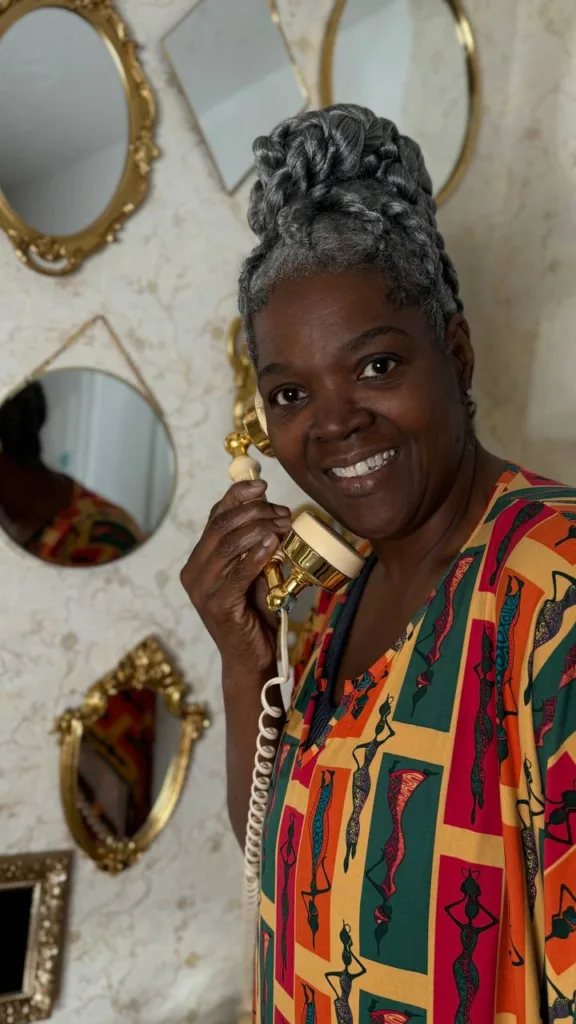 Mujer sonriente usando un teléfono dorado vintage en un espacio decorado de Charm Home Miami